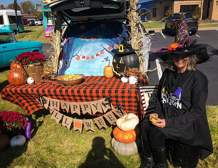 M1 Credit Union Trunk or Treat event raising funds for Adopt-a-Family Christmas gifts, with staff in festive costumes engaging the community